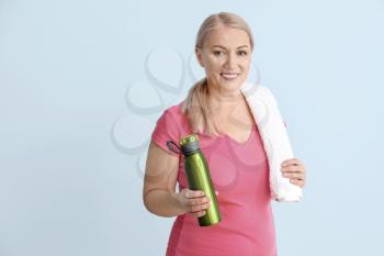 Sporty mature woman with bottle of water on color background�
