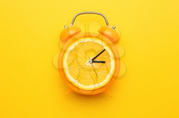 Creative alarm clock with citrus fruit on color background�
