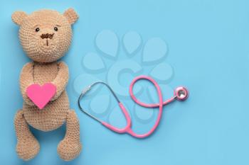 Stethoscope, baby toy and heart on color background�