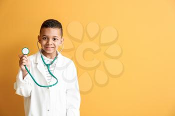 Cute little African-American doctor on color background�