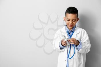 Cute little African-American doctor on light background�