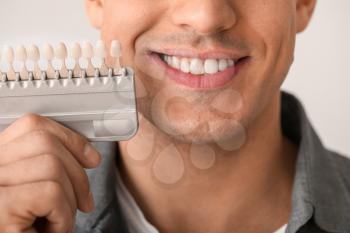 Man with teeth color samples on light background, closeup�