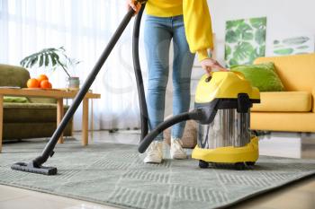 Young woman hoovering floor at home�