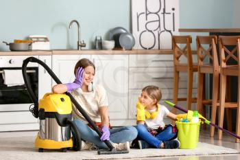 Young woman and her little daughter with vacuum cleaner in kitchen�