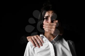 Angry husband covering mouth of his wife on dark background. Concept of domestic violence�