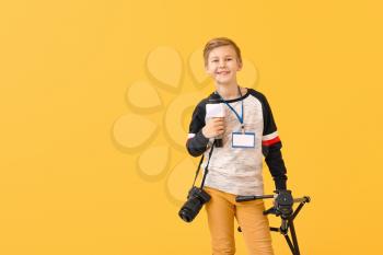 Little journalist with microphone and camera on color background�