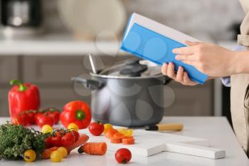 Woman with cook book preparing food in kitchen�