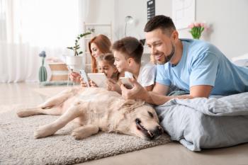 Happy family with modern devices and dog in bedroom at home�