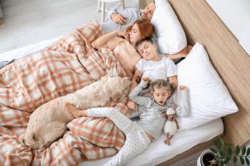 Happy family with dog sleeping in bed at home�
