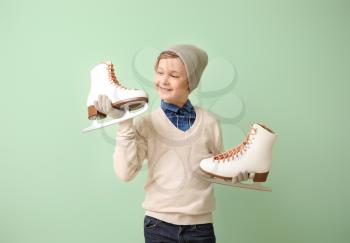 Cute little boy with ice skates against color background�