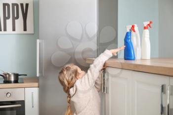 Little girl trying to reach out for bottles of detergent at home�