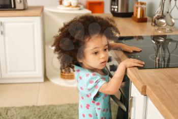 Little African-American girl playing with stove in kitchen. Child in danger�
