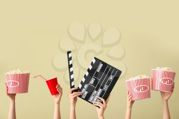 Many hands with popcorn, drink and movie clapper on color background�