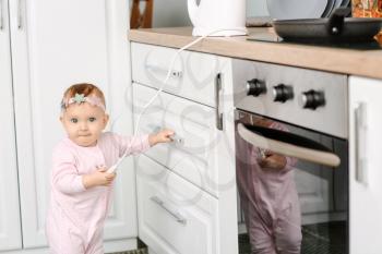 Little baby playing with electric plug in kitchen. Child in danger�