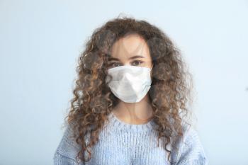 Young woman with protective mask on light background. Concept of epidemic�