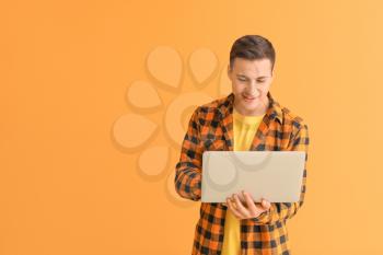 Young man with laptop checking his e-mail on color background�