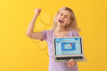Happy young woman with laptop checking her e-mail on color background�