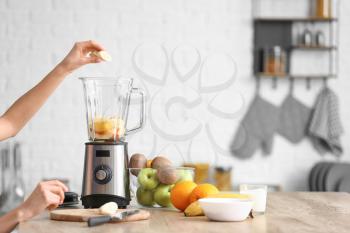 Young woman making fruit smoothie in kitchen at home�