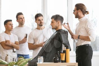 Professional hairdresser teaching young men in salon�
