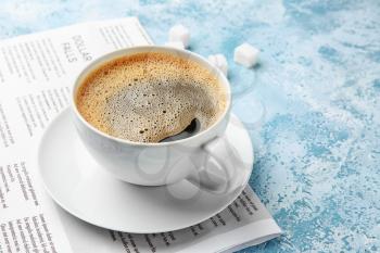 Cup of hot coffee and newspaper on color background�