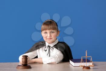 Portrait of little judge sitting at table against color background�