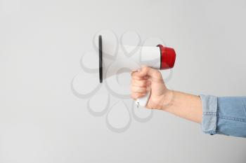 Male hand with megaphone on light background�