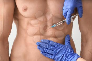Muscular man receiving injection of steroids on light background, closeup�