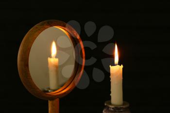 Glowing candle near mirror on dark background�