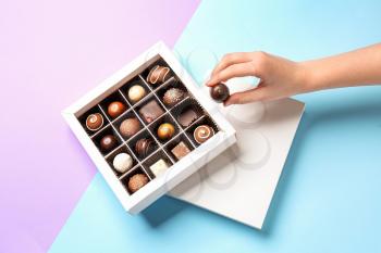 Woman taking chocolate candy from box on color background�