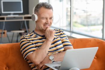 Mature man with laptop and headphones sitting on sofa at home�