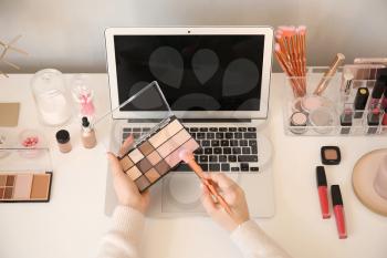 Makeup artist at table with modern laptop and cosmetics�