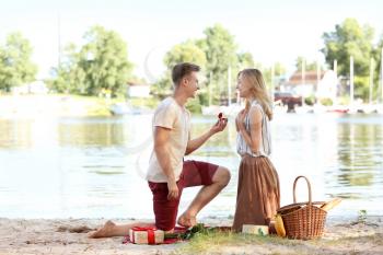 Young man making proposal to his girlfriend on romantic date near river�