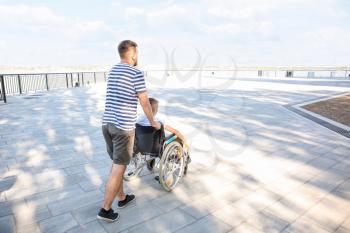 Teenage boy in wheelchair with his father walking outdoors�
