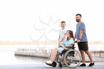 Young woman in wheelchair with her family walking outdoors�