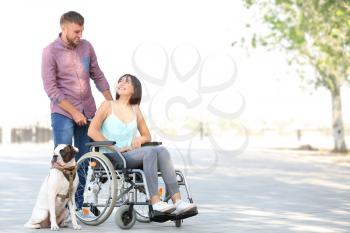 Young woman in wheelchair with her husband and service dog outdoors�