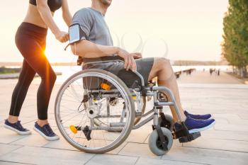 Sporty woman helping young man in wheelchair outdoors�