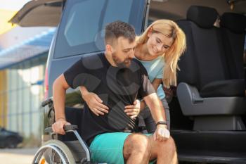 Woman helping handicapped man to sit in car�