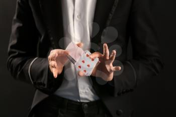 Magician showing tricks with cards on dark background, closeup�