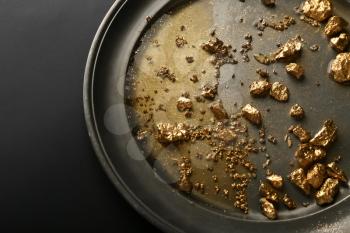 Plate with gold nuggets on black background�