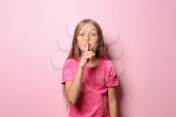 Little girl in t-shirt showing silence gesture on color background�