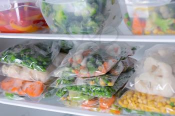 Plastic bags and containers with frozen vegetables in refrigerator�