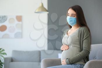Pregnant woman wearing medical mask at home�