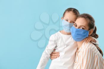 Little daughter with her mother in protective masks on color background�