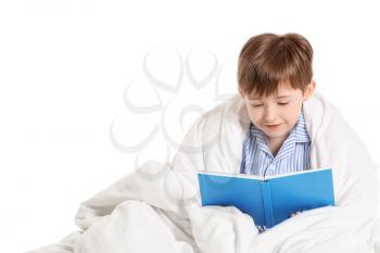Little boy wrapped in blanket reading book on white background�