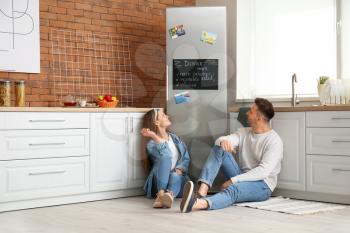 Happy couple sitting on floor near refrigerator in kitchen�