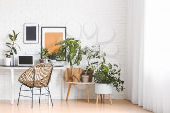 Comfortable workplace with modern laptop and houseplants near white brick wall�