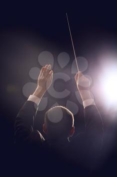 Male conductor on dark background, back view�