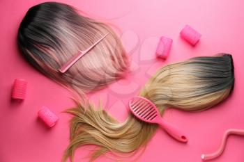 Female wigs, brush, comb and curlers on color background�
