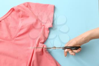 Woman cutting t-shirt on color background�