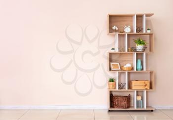 Wooden rack with decor near color wall in room�